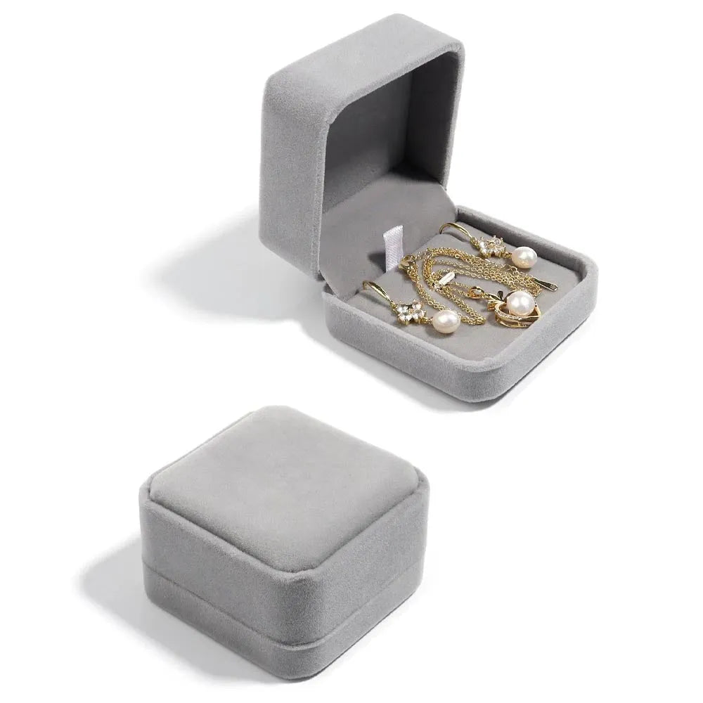 Grå sammetspresentbox med mjuk inredning som håller guldfärgade pärl och diamantörhängen