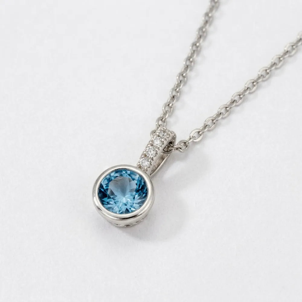 En delikat silverhalsband med en rund isblå sten och små diamanter längs infattningen called blue ivy