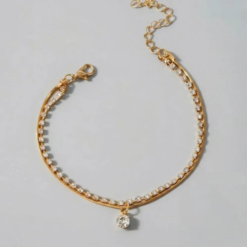 Guldtonad fotlänk med dubbla kedjor prydd med klara strass och hängande kristallpendel celia