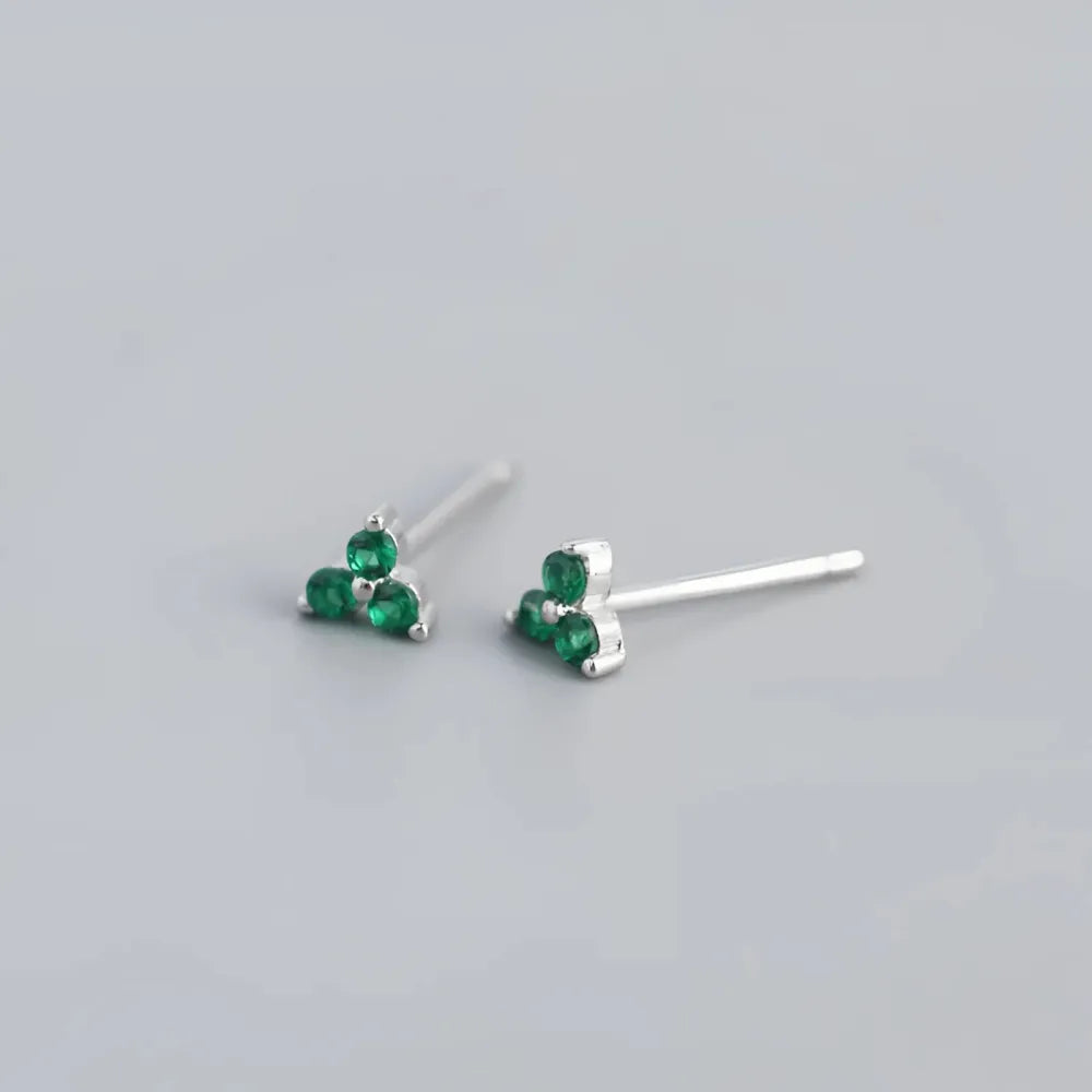 Silverörhängen med små studs franka tre gröna smaragdstenar arrangerade i en triangel