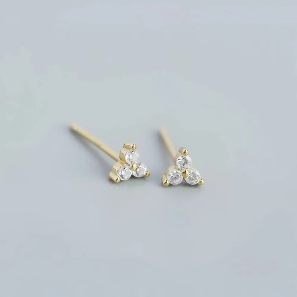 Delikata guldfärgade triangelformade små studs med tre klara glittrande cubic zirconia stenar franka