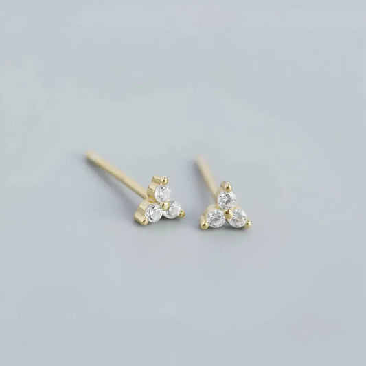 Delikata guldfärgade triangelformade små studs med tre klara glittrande cubic zirconia stenar franka