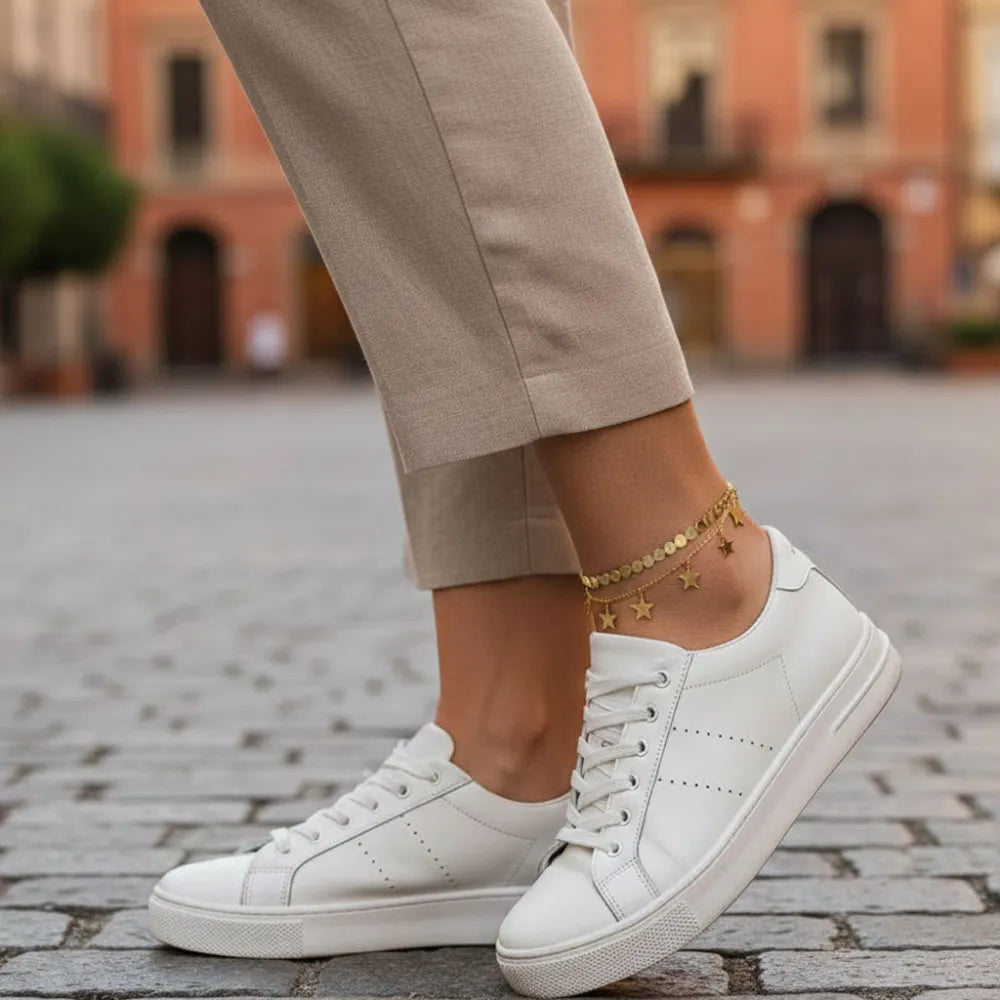 Vita lädersneakers med perforerad detailing och minimalistisk design kopplade till grethe fotlänk med dubbla kedjor och stjärnor