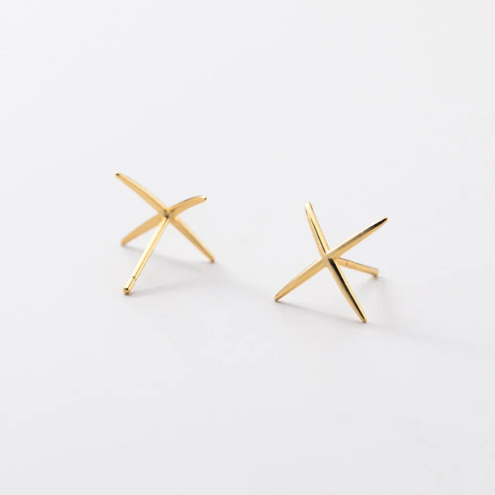 Loomi guldfärgade minimalistiska stjärnformade stiftörhängen med slät metallisk yta och kryssdesign