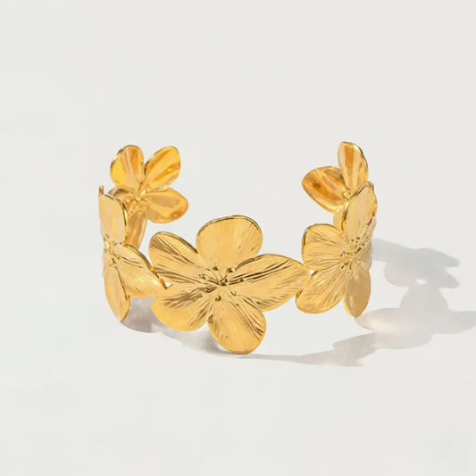 Goldtonad magnolia-armring i metall med stora blommor och detaljrik kronbladsdesign
