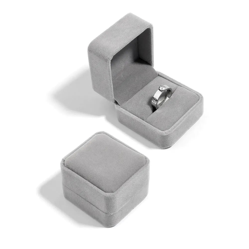 En elegant silverring med en diamant i bandet liggande i en öppen sammetsskatt presentbox i mjukt grå sammet