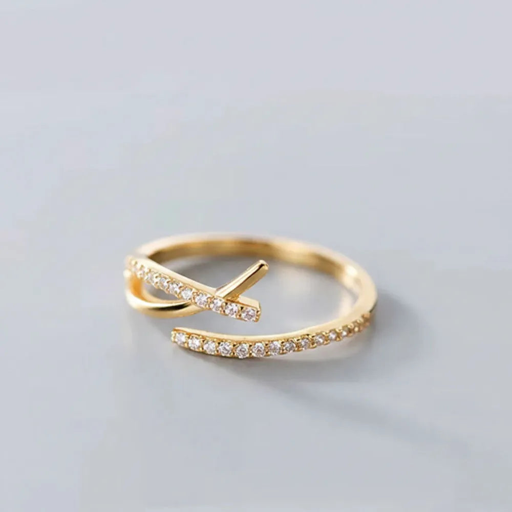 Sivra justerbar ring i guld med böljande form och glittrande klara stenar på bandet