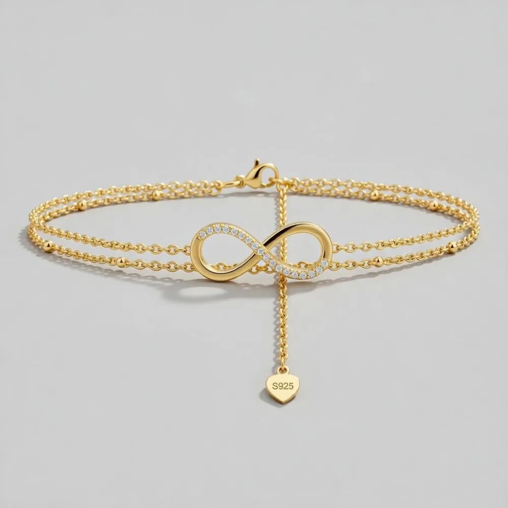 Timeless fotlänk med dubbla kedjor i guld och infinitysymbol med infattade diamanter och hjärtberlock s925