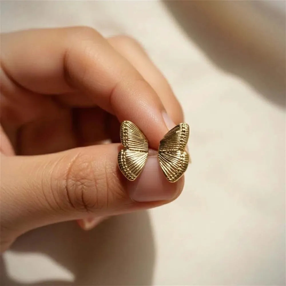 Goldfärgade fjärilsformade studs med intrikat räfflade vingdetaljer winga studs med fjärilsvingar