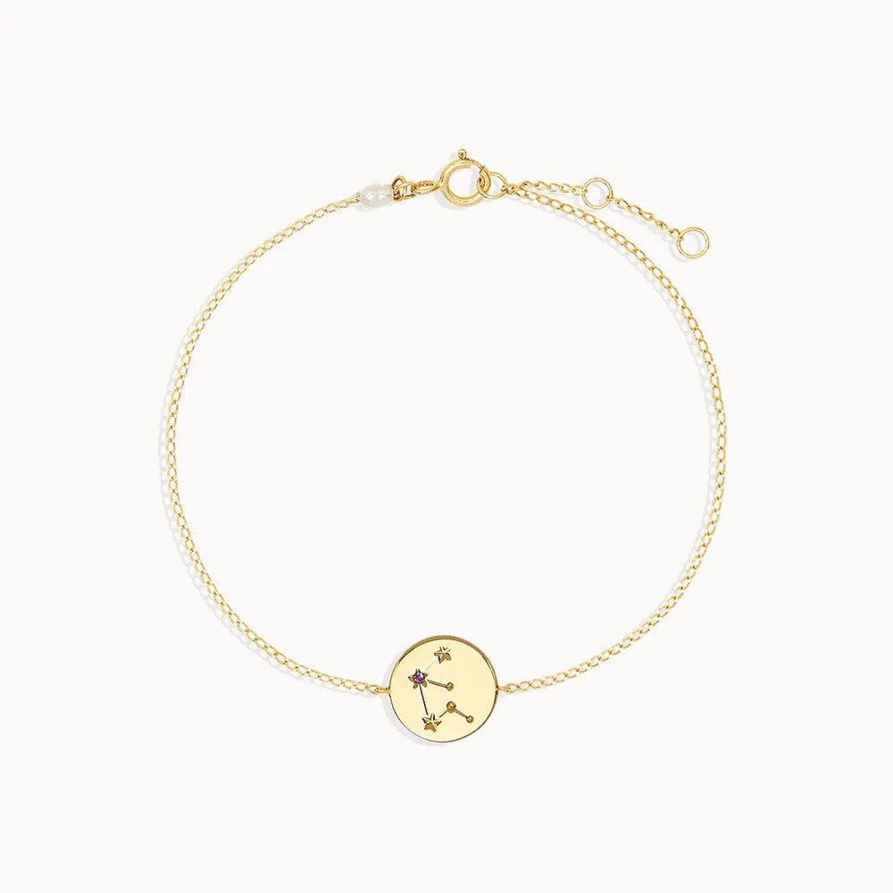 Zodiac sign armband med stjärntecken i guldfärgad metall och cirkulär berlock med ingraverad konstellation och lila sten