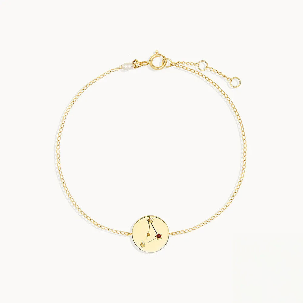 Goldtonat armband med cirkulär berlock och ingraverad stjärnteckendesign med liten röd ädelsten