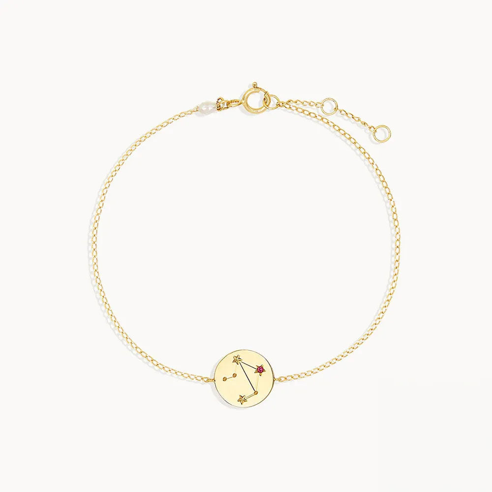 Zodiac sign armband i guldton med stjärnteckendesign och röd ädelsten på cirkulärt hänge